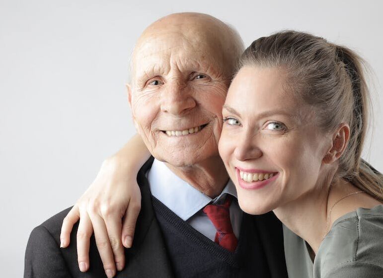 Cheerful elderly man and adult woman cuddling on white background and looking at camera