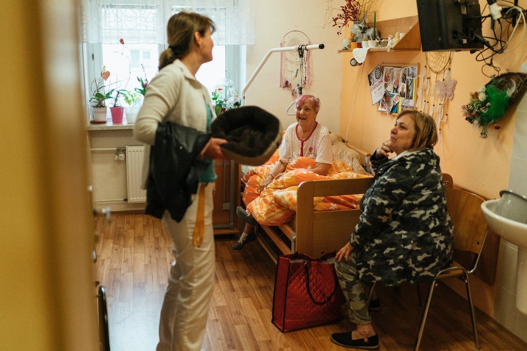 Pečovatelka hovoří v pokoji se seniorkou a její návštěvou